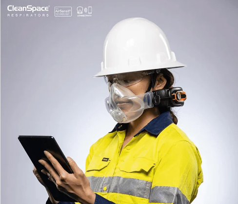 Worker wearing CleanSpace respirator and helmet using tablet for safety compliance.