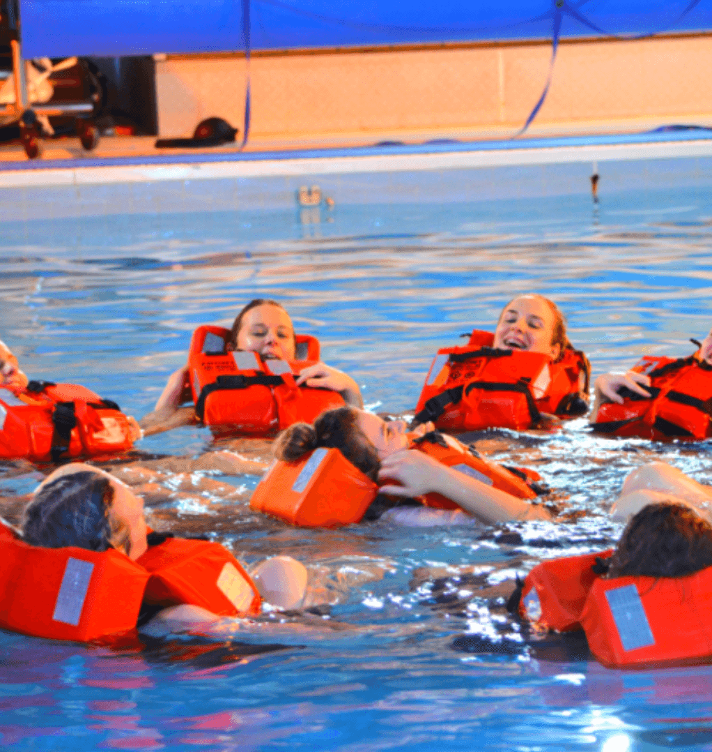 Group of trainees wearing life jackets practicing water survival skills in a pool during STCW Basic Safety Training Course. Essential for maritime safety compliance.