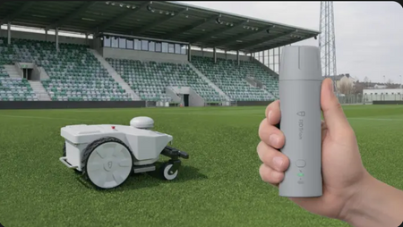 Hand holding remote control for robotic mower on field